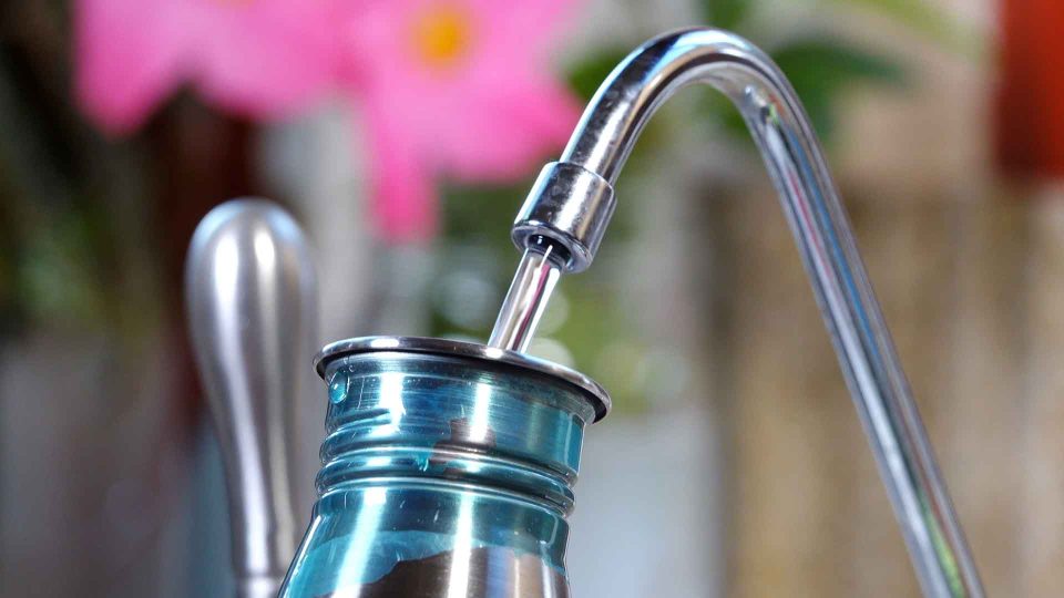 Close up filling reusable metal water bottle at reverse osmosis faucet - no need for disposable plastic